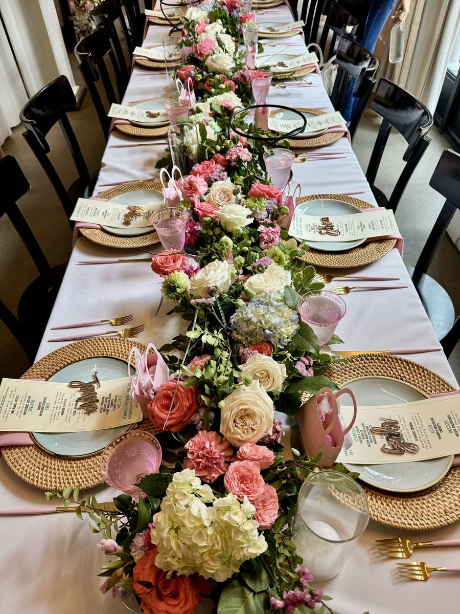 A long table set with a floral runner and rattan chargers.